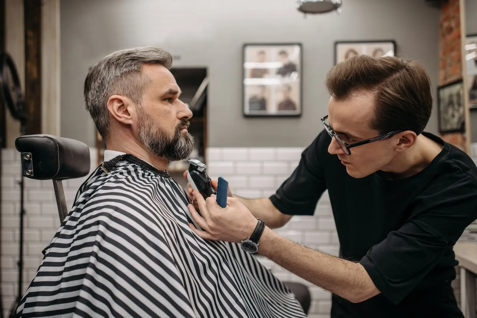 Barber trimming a client beard in a patterned cape